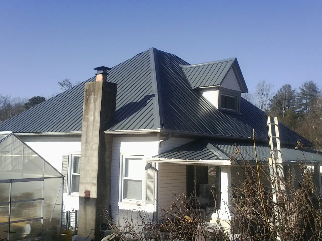Dark blue standing seam metal roof on a white farmhouse with dormer — Slate & Tile Roof Repair by Roofing Brothers in Granby