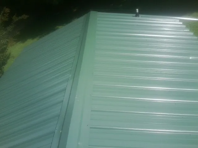 New green metal panels meeting at the ridge of a roof — Flat Roof Repair work by our crew in Granby